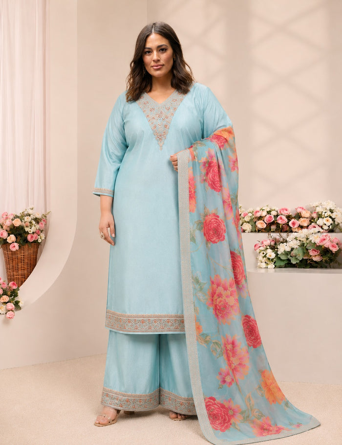 A woman models a light blue traditional Indian salwar kameez suit with a matching floral dupatta. The suit features a light blue kurta with gold embroidery on the neckline and borders, paired with matching wide-leg trousers.