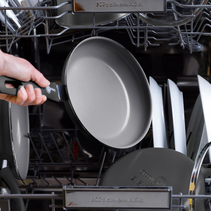 Hand loading a Dover ceramic nonstick frypan into a dishwasher with other cookware.