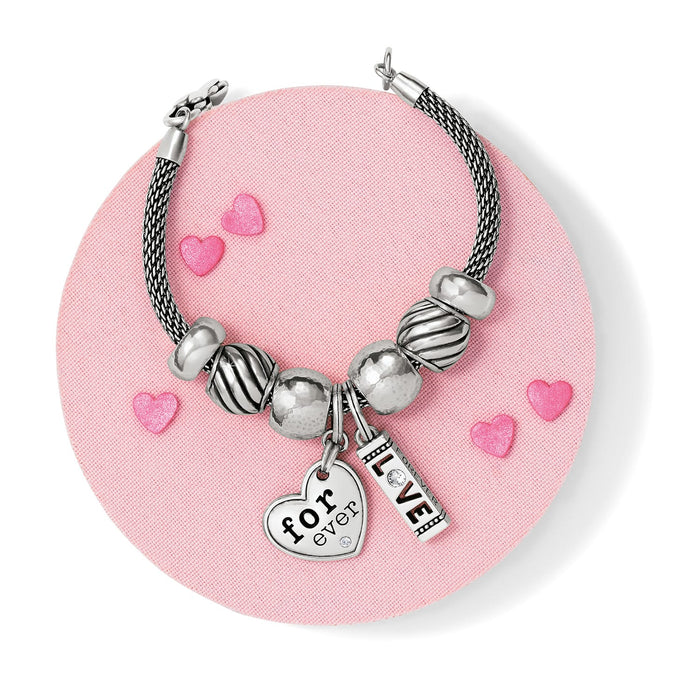 Brighton silver-plated beaded charm bracelet styled with heart and love charms on a pink background
