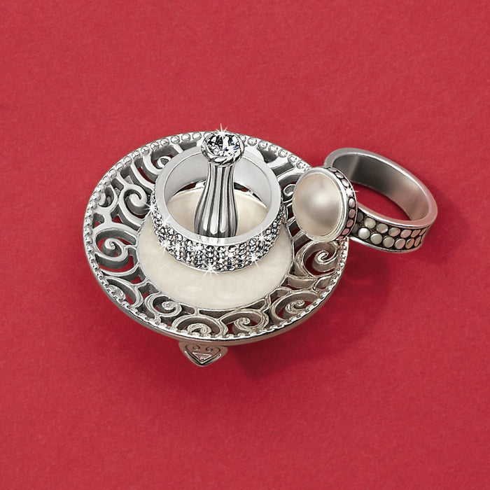 Brighton ring holder with silver-tone scrollwork base and crystal-accented top, displaying a pearl ring on a red background