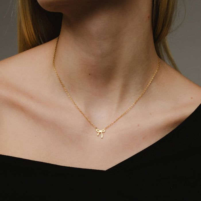 Gold necklace with a bow pendant worn by a person against a neutral background