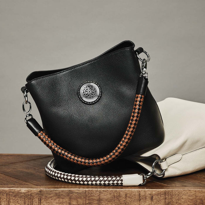 Brighton black leather handbag styled with a white leather bag and braided straps on a wooden surface
