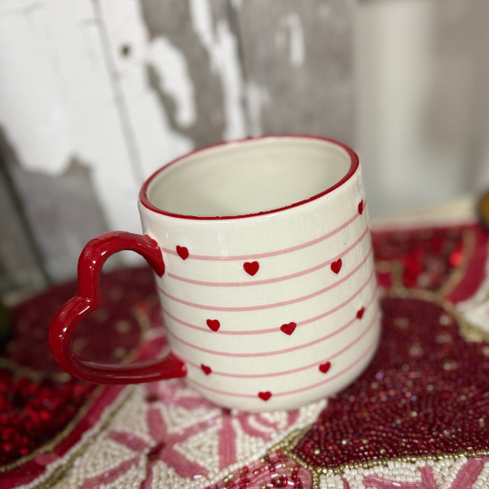 White mug with red heart patterns on a decorative surface with pink and red patterns.