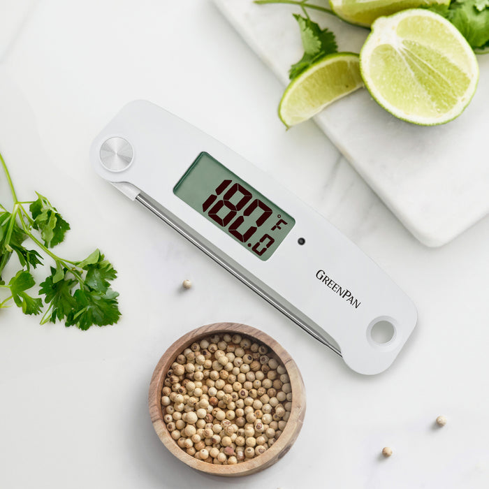 Digital kitchen thermometer displaying 180°F on a countertop with herbs, lime slices, and white peppercorns nearby.