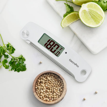 Digital kitchen thermometer displaying 180°F on a countertop with herbs, lime slices, and white peppercorns nearby.
