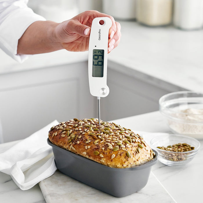 Digital kitchen thermometer measuring the temperature of a seeded loaf in a metal bread pan.