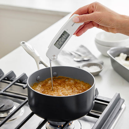 Hand holding digital kitchen thermometer in bubbling pot on stove, display reads 224.8°F.