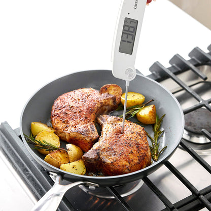 Hand using a digital kitchen thermometer to check pork chops and potatoes cooking in a skillet.