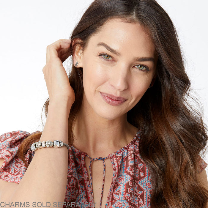 Model wearing a Brighton silver-plated charm bracelet with ornate beads and crystal accents paired with matching stud earrings