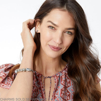 Model wearing a Brighton silver-plated charm bracelet with ornate beads and crystal accents paired with silver stud earrings