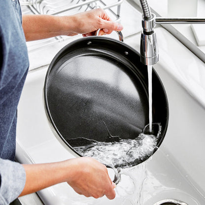 Person washing a Bistro 12-inch electric skillet under running water in a kitchen sink.