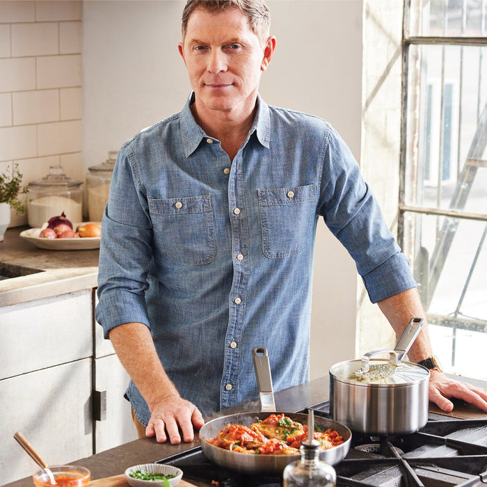Man in a blue shirt cooking on a stove with stainless steel Bobby Flay by GreenPan cookware set.