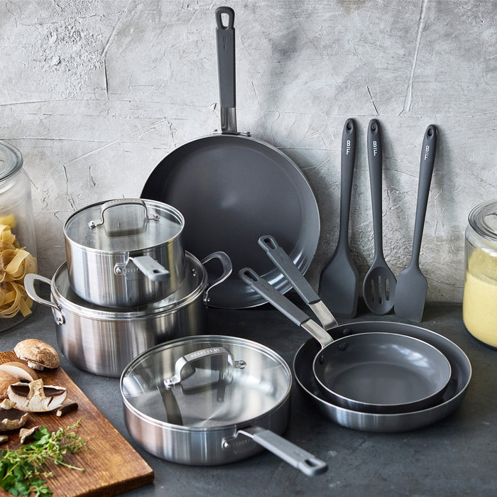 12-piece stainless steel cookware set with pots, pans, and a black frypan displayed on a kitchen counter.