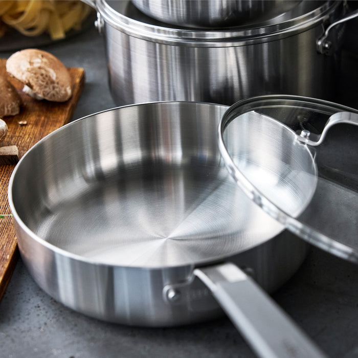 Stainless steel frypan with glass lid on counter next to chopped mushrooms.