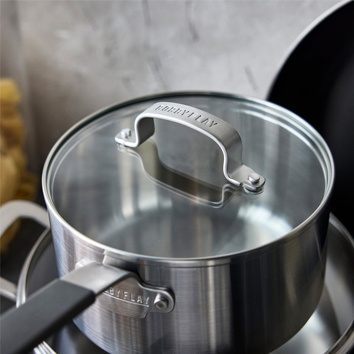 Stainless steel saucepan with glass lid and a nonstick frypan from a 12-piece cookware set on a stovetop.