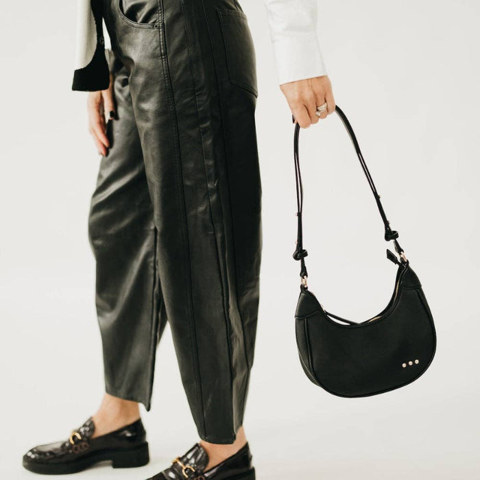 Person wearing black leather pants and holding a black handbag on a white background