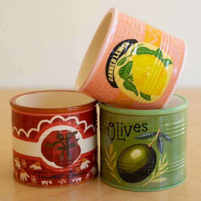 Three decorative tins with fruit and olive designs on a wooden surface.
