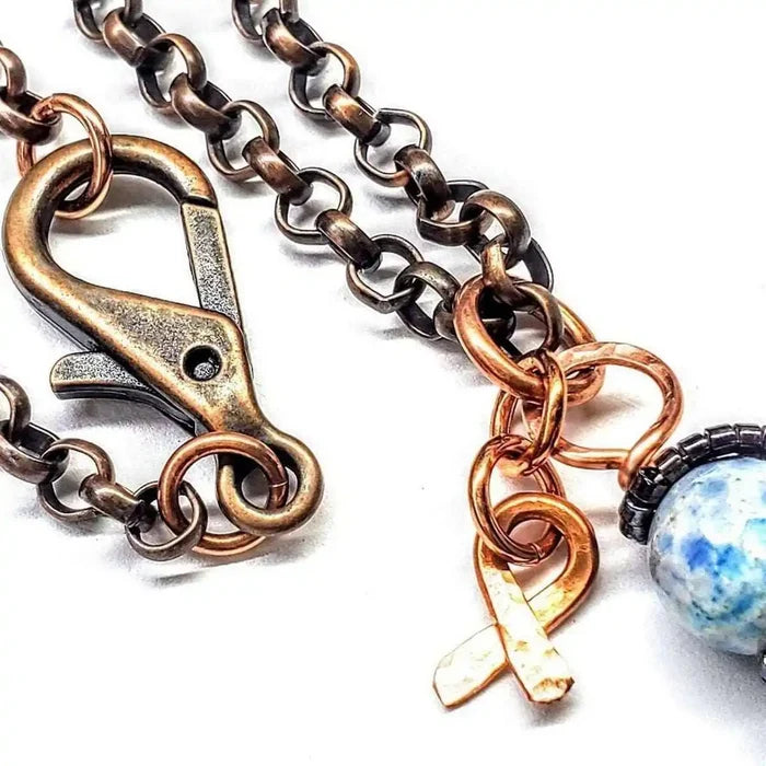 Close-up of the clasp and copper awareness ribbon on the Child Abuse Awareness Agate Necklace With Lava Rock Bead.