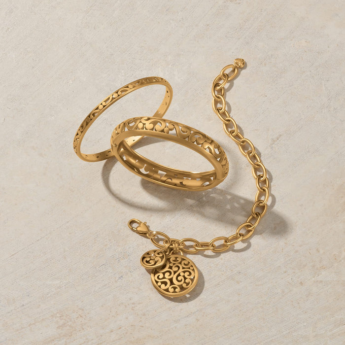 Brighton gold-plated bangles styled with a matching charm bracelet featuring scroll cutout medallions on a neutral background