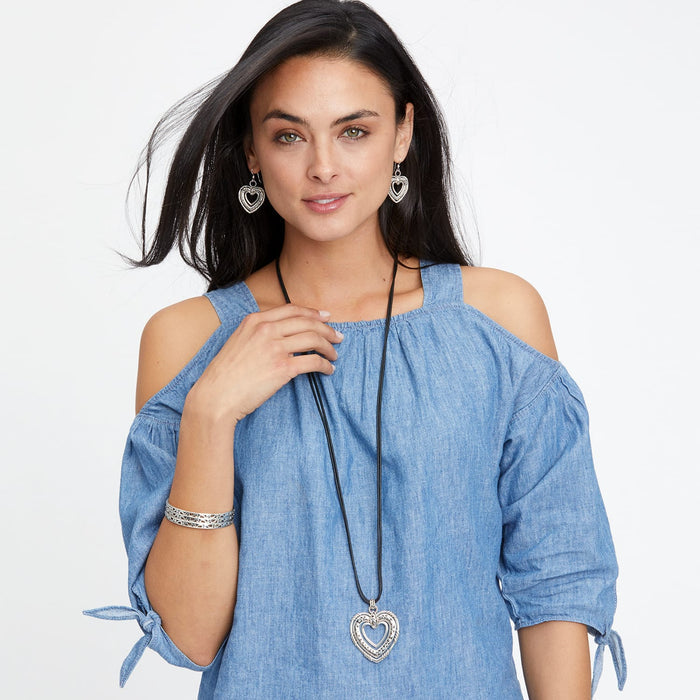 Model wearing a Brighton silver-plated heart pendant necklace on black cord with coordinating heart drop earrings and bracelet
