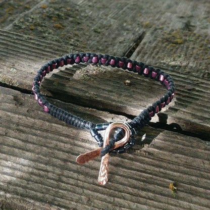 Copper Ribbon Black Pink Braided Breast Cancer Bracelet on a wooden surface showcasing its unique design and features.