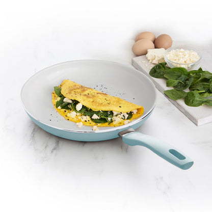 Blue ceramic nonstick 10-inch frypan with spinach and cheese omelet, eggs, spinach, and cheese beside the pan.