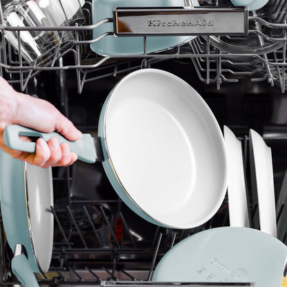 Blue ceramic nonstick frypan being placed into a dishwasher with other cookware and dishes.
