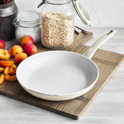 Cream white ceramic nonstick frypan with stay-cool handle, placed on a surface next to apricots, oats, and sugar.