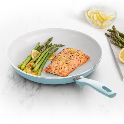 Salmon, lemon, and asparagus in a blue ceramic nonstick frying pan on a white surface.