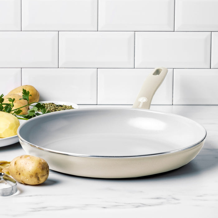 Cream white ceramic nonstick 12-inch frypan on white countertop with potatoes and parsley beside it.