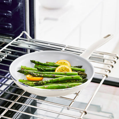 Cream white ceramic 12-inch frypan on oven rack, holding asparagus spears and lemon slices.