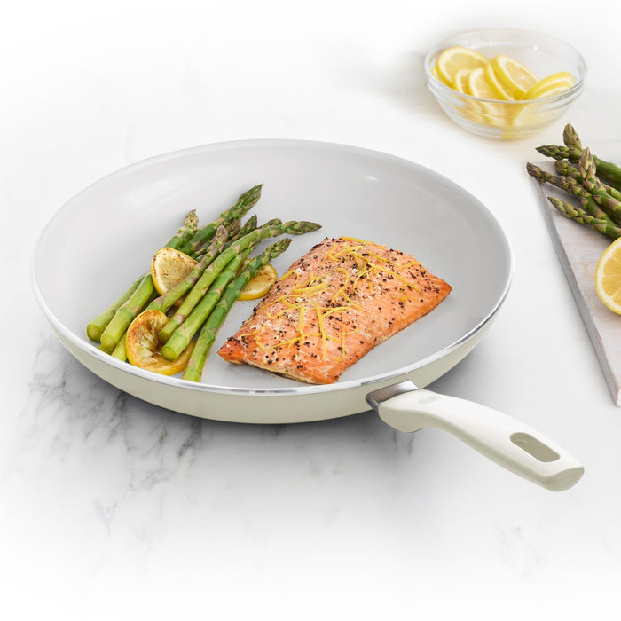 Cream white ceramic 12-inch frypan with salmon, asparagus, and lemon slices on a white countertop.