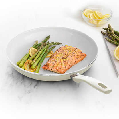 Cream white ceramic 12-inch frypan with salmon, asparagus, and lemon slices on a white countertop.