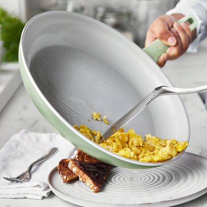 Scrambled eggs being served onto toast from a white Dover ceramic nonstick frypan with a spatula.