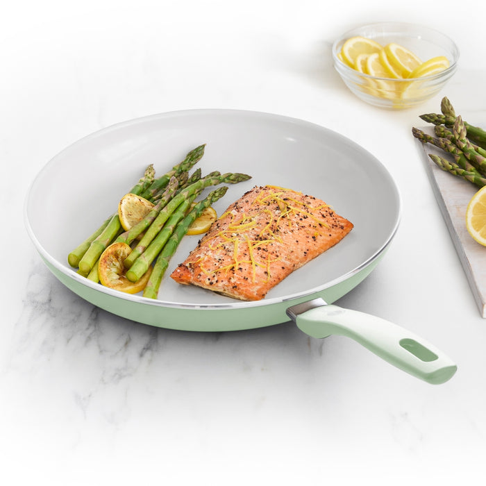 Salmon, asparagus, and lemon slices in a pastel green ceramic nonstick frypan with garnishes on the side.