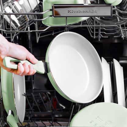 Pastel green ceramic nonstick frypan being loaded into a dishwasher alongside other dishes.
