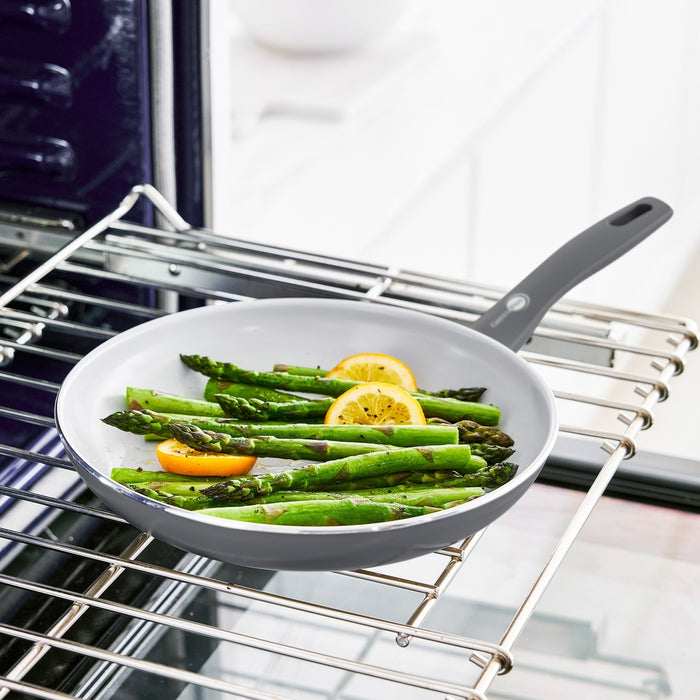 Charcoal gray 12-piece ceramic cookware set with asparagus and lemon on an oven rack.