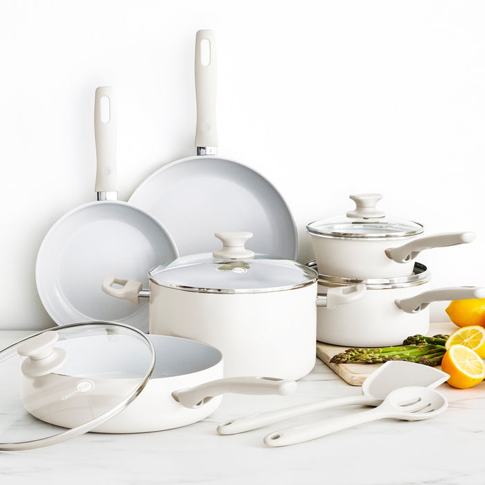 Cream white ceramic cookware set with multiple pots, pans, lids, and utensils arranged together, 12 pieces shown.