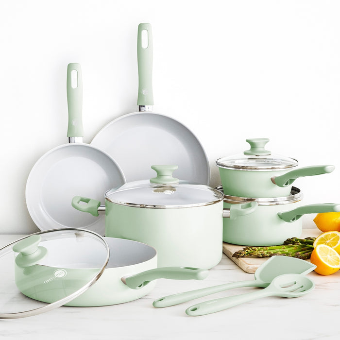 Pastel green 12-piece ceramic cookware set with pots, pans, lids, and utensils arranged on a white countertop.