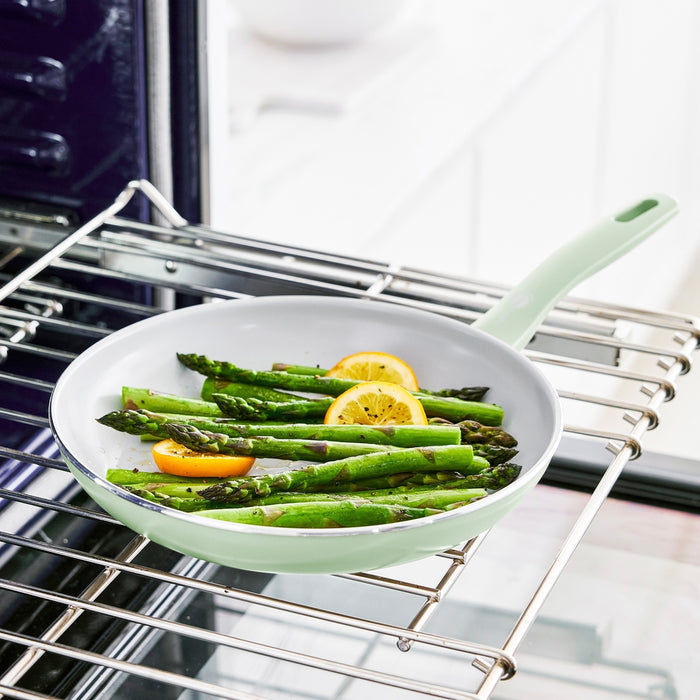 Pastel green 12-piece ceramic nonstick cookware set with asparagus and lemon on an oven rack.