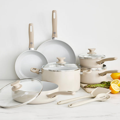 Taupe ceramic nonstick 12-piece cookware set with pots, pans, glass lids, and cooking utensils arranged together.
