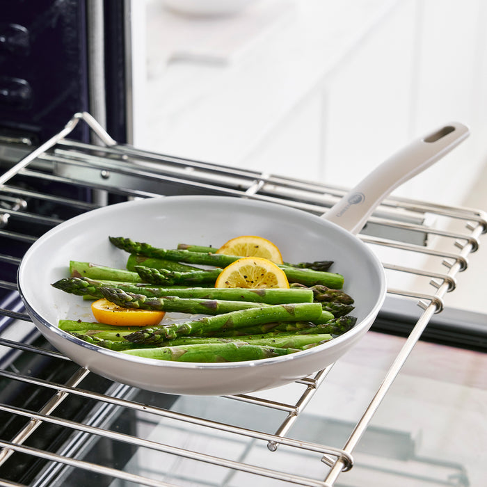 Taupe ceramic nonstick pan from 12-piece set on an oven rack, holding asparagus and lemon slices.
