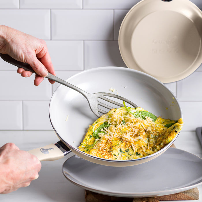 A hand folds a spinach and cheese omelette with a spatula in a gray Dover ceramic nonstick frying pan.