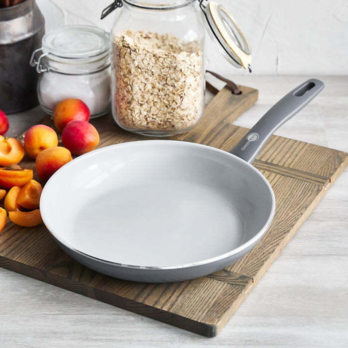 Ceramic nonstick frypan set on a wooden board with apricots and a jar of oats nearby.