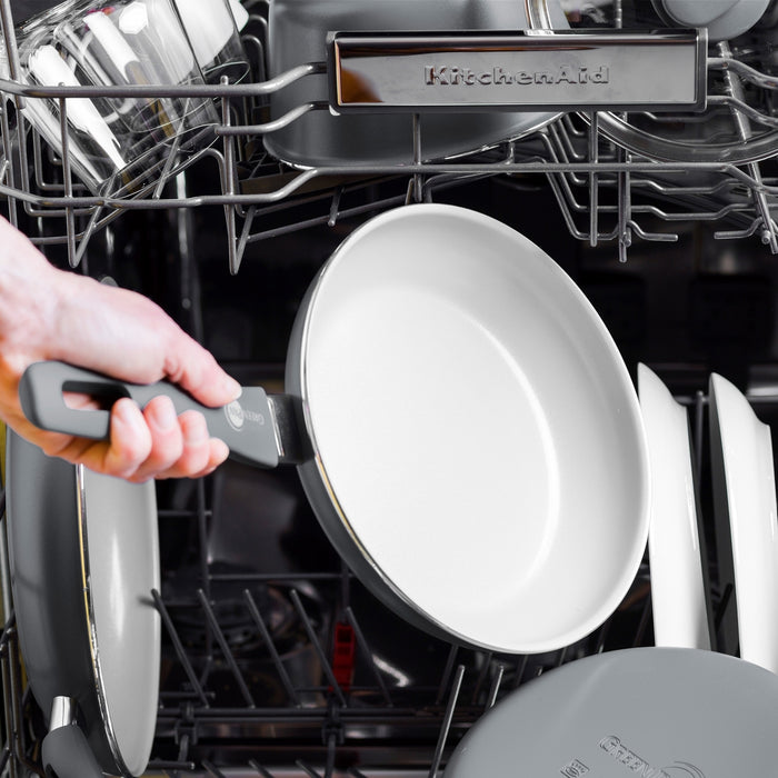 Hand placing a Dover ceramic frypan into a dishwasher with other kitchenware; part of an 8, 10, and 12 set.