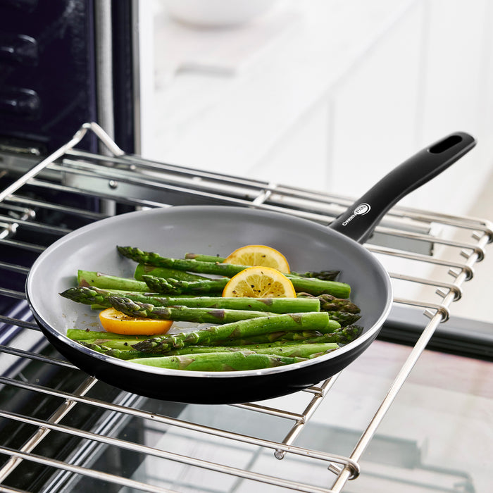 Asparagus and lemon slices in a white ceramic nonstick frypan on an oven rack.