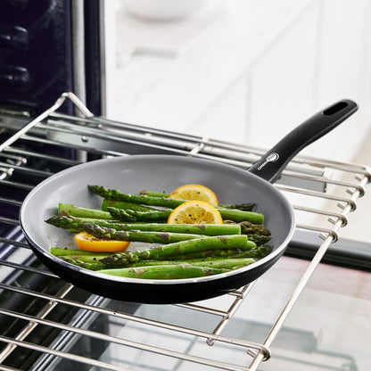 Asparagus and lemon slices in a white ceramic nonstick frypan on an oven rack.