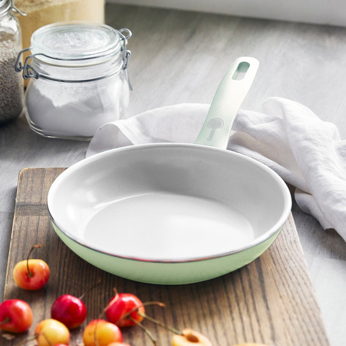 Pastel green ceramic nonstick frypan set, 8 and 10, on wooden board with cherries and flour nearby.