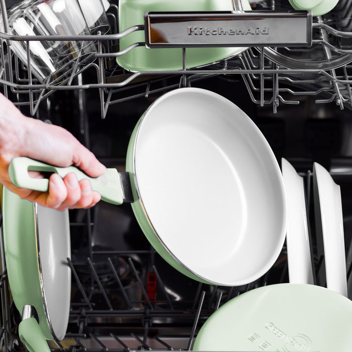 Pastel green ceramic nonstick 8 and 10 frypan set being placed in a dishwasher with other dishes and cookware.