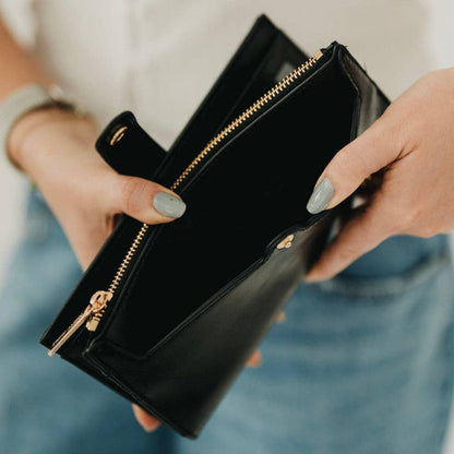 Black clutch with gold zippers held by a person with light blue jeans.